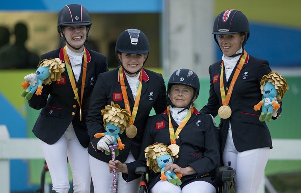 Four people in equestrian outfits holding the Rio 2016 mascot and wearing gold medals