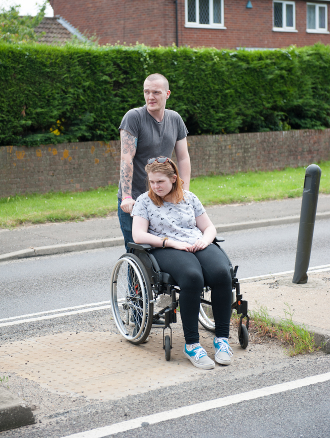 A man pushing a woman in wheelchair across a road