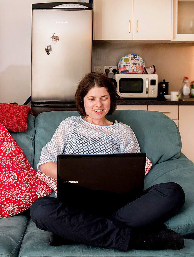 A smiling woman sitting on a sofa with a laptop in her home