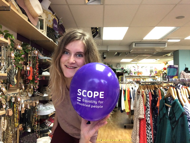 Volunteer Jekaterina Starovoitova in a charity shop holding a purple Scope balloon
