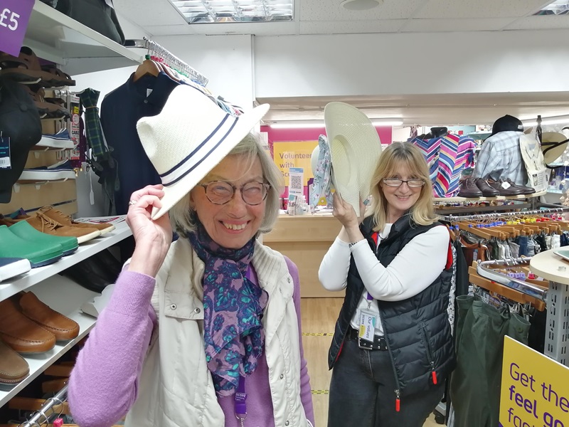 Volunteer Linda Anderson poses with a white straw hat in a Scope shop. Linda has a big smile and looks like she's having fun.