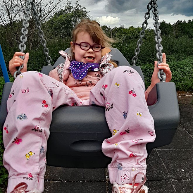 A smiling girl on an accessible swing in a playground